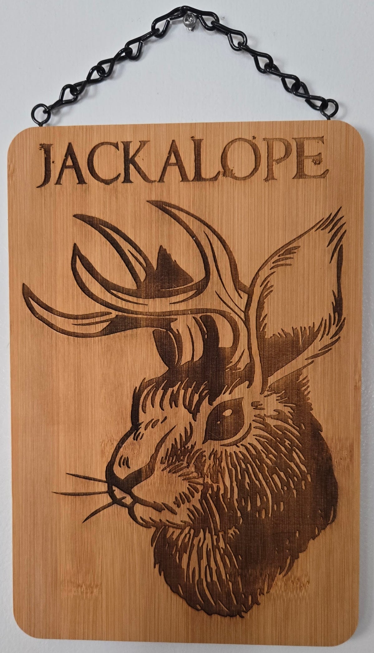 A wooden plaque with a carved image of a rabbit or deer head, and the word "JACKALOPE" written above it.