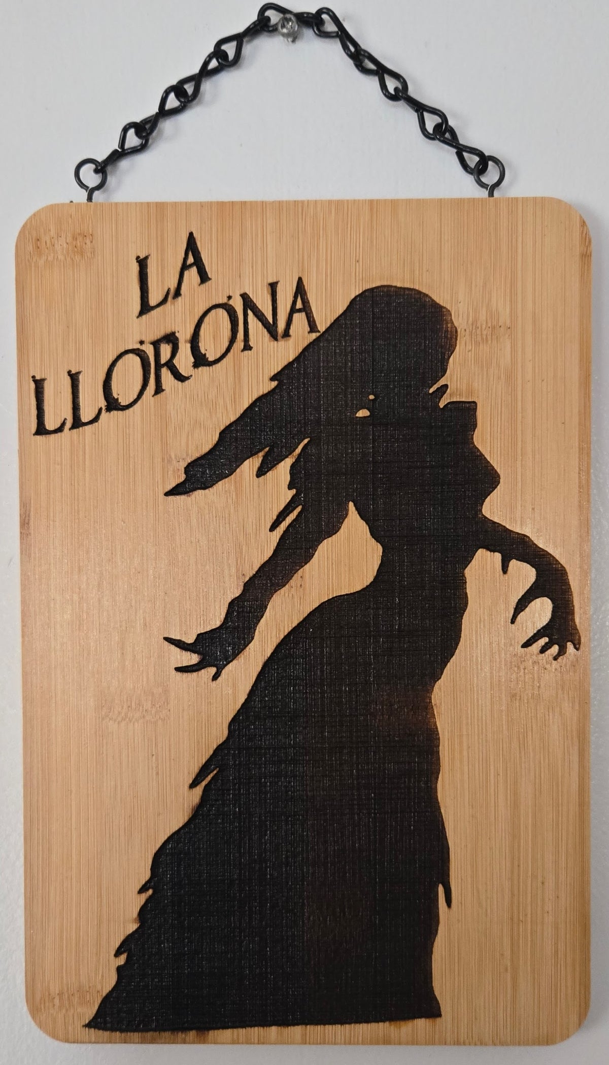 a wooden sign with a silhouette of a person, possibly a woman, and the text "La lloration" written above it.