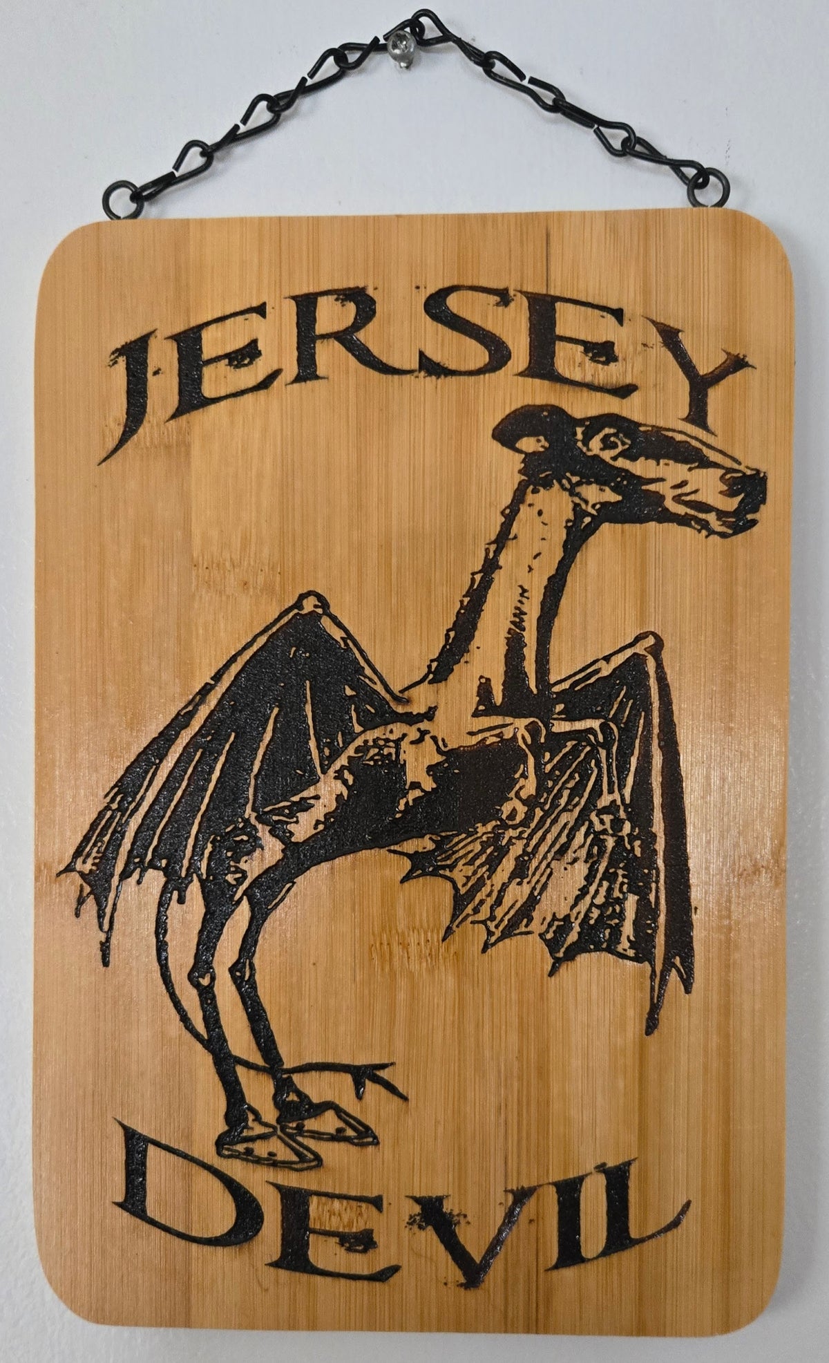 a wooden sign with a bat-like creature and the text "JERSEY DEVIL" printed on it.