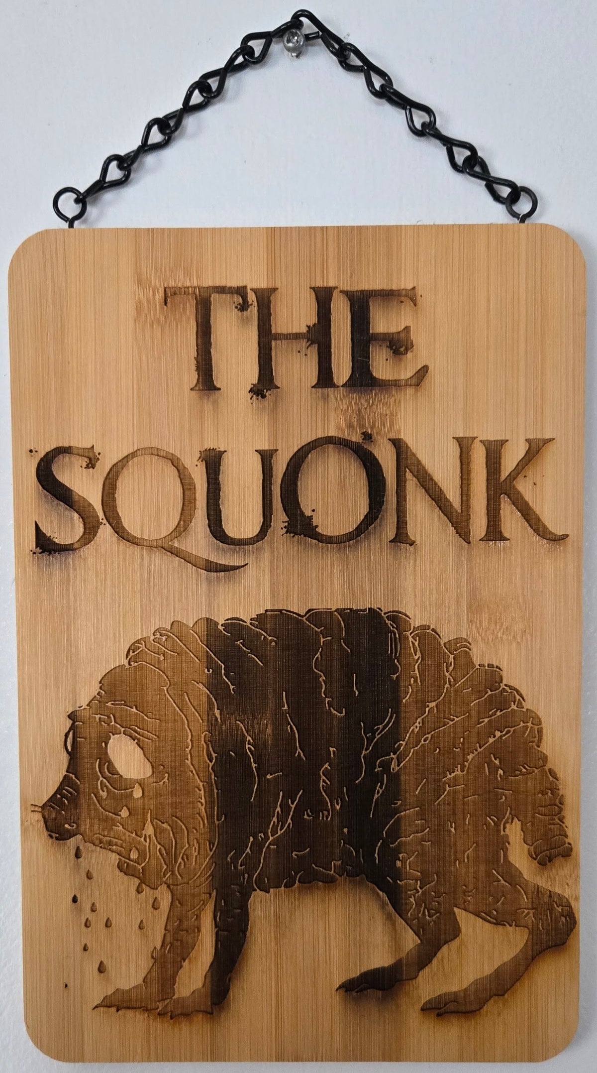 a wooden plaque with the text "THE SQUONK" and an illustration of a bear.